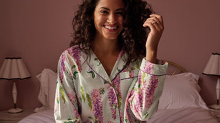 Model Wears Wisteria print Pyjamas,as while sat smiling on a bed