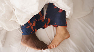 feet touch in bed, white sheets, lobster print pyjamas