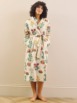 Woman wearing a floral robe dressing gown standing in a room with a plain wall.