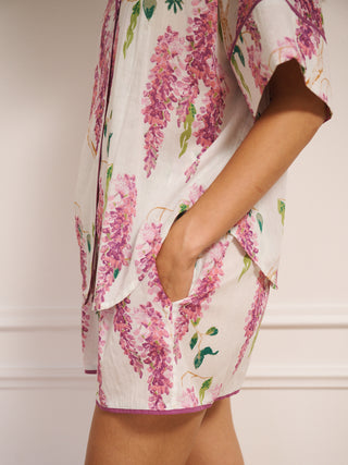 Model wearing white cotton voile oversized shortie pyjamas with pink wisteria print, short-sleeve shirt and elasticated waist shorts with pockets. side detail