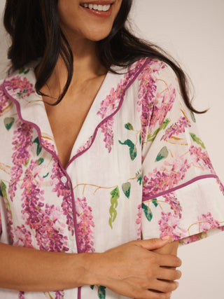 Model wearing white cotton voile oversized shortie pyjamas with pink wisteria print, short-sleeve shirt and elasticated waist shorts with pockets.