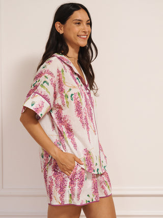 Model wearing white cotton voile oversized shortie pyjamas with pink wisteria print, short-sleeve shirt and elasticated waist shorts with pockets.