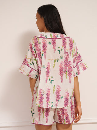 Model wearing white cotton voile oversized shortie pyjamas with pink wisteria print, short-sleeve shirt and elasticated waist shorts with pockets. back detail