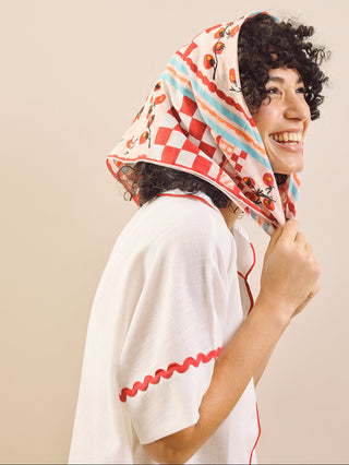 Woman wearing a colorful headscarf and white top against a beige background