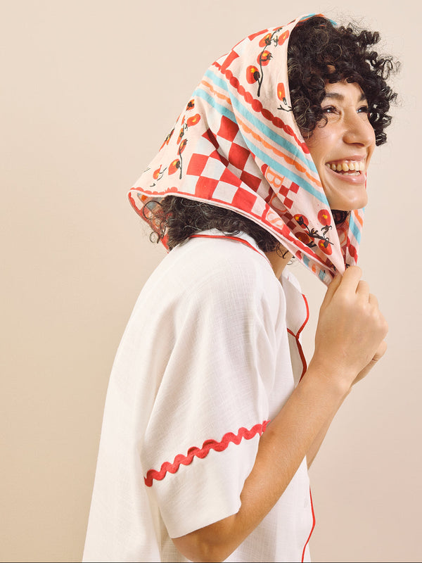 Woman wearing a colorful headscarf and white top against a beige background