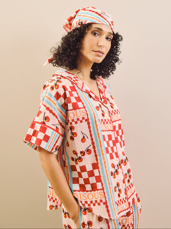 Woman wearing a bandana and red and white checkered pyjamas with cherry patterns on a beige background