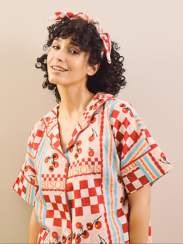 Woman wearing a colorful patterned shirt with a headscarf against a beige background