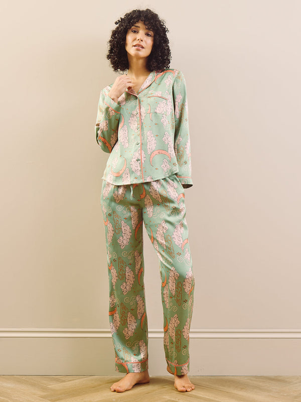 Person wearing a green pyjama set with a pattern in a room with a beige wall and wooden floor.