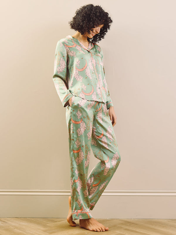 Woman wearing a green floral pyjama set against a beige wall.