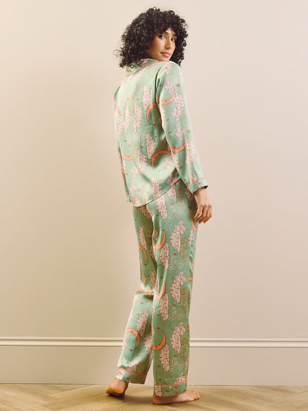 Woman wearing a green floral and moon pyjama set against a plain background