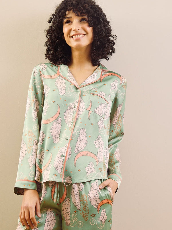 Woman wearing a green floral and moon pyjama set against a beige background