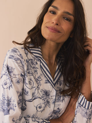Woman wearing a white pyjamas with blue floral patterns against a beige background