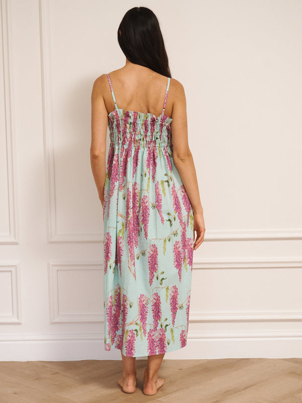 Model wearing a duck egg blue cotton cami midi night dress with pink wisteria print, featuring a shirred bodice and thin straps. Back detail. 