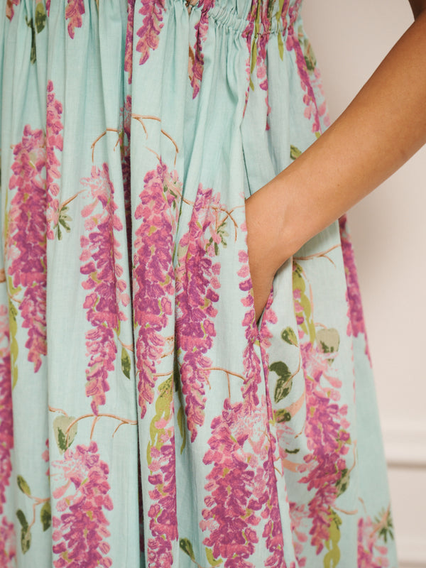 Model wearing a duck egg blue cotton cami midi night dress with pink wisteria print, featuring a shirred bodice and thin straps. pocket detail