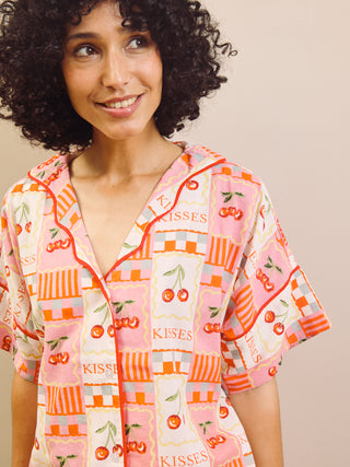 Woman wearing a colorful patterned pyjama shirt with 'Kisses' text and cherry design.