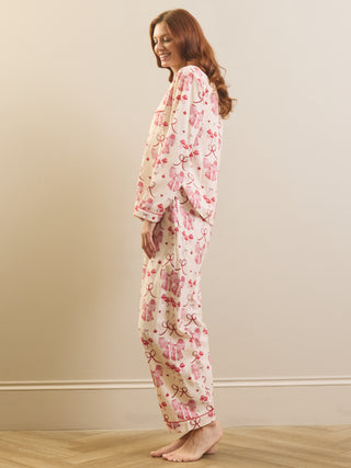 A woman wearing a two-piece pyjama set with a pink and red floral print on a cream background, standing in profile against a beige wall.