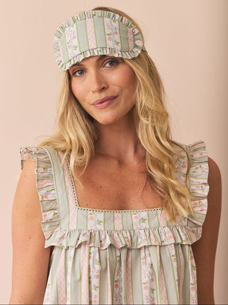 Woman wearing a matching eye mask and dress with floral and striped pattern on a pink background