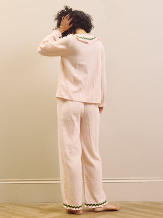 Person wearing a light pink pyjama set with green trim against a plain wall.