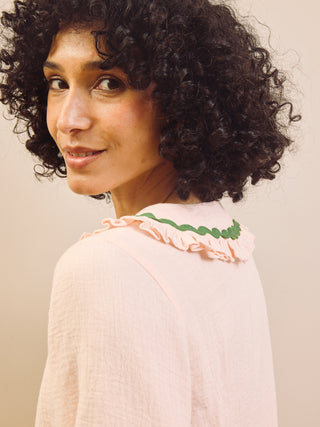 Woman with curly hair wearing a light pink pyjama top with green trim on a beige background