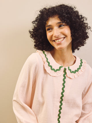 Woman wearing a light pink pyjama top with green trim against a beige background