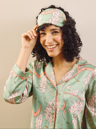 model wears sage green pyjamas and eye mask agains a beige background