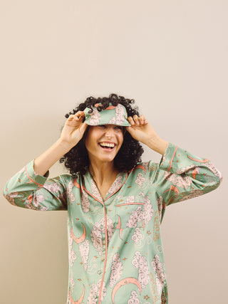 model wears sage green pyjamas and eye mask agains a beige background