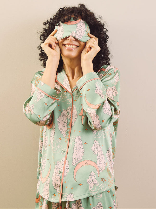 model wears sage green pyjamas and eye mask agains a beige background