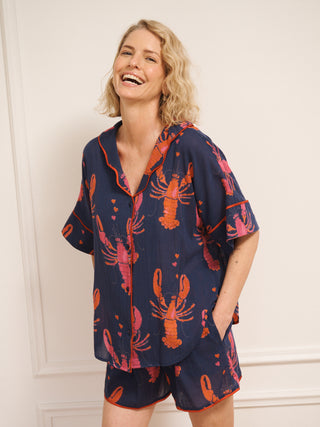 Model wearing navy gauze shortie pyjamas with a playful lobster and heart print, featuring a relaxed short-sleeve button-up shirt and matching shorts.