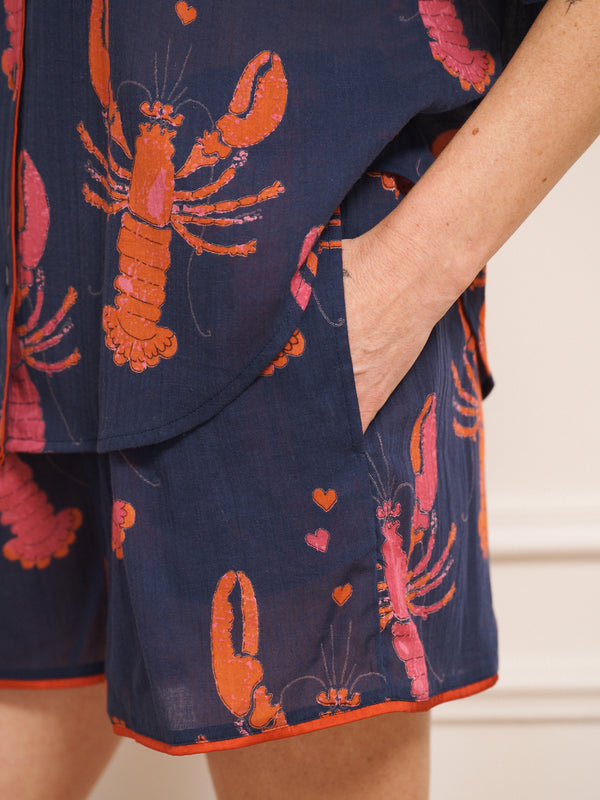 Model wearing navy gauze shortie pyjamas with a playful lobster and heart print, featuring a relaxed short-sleeve button-up shirt and matching shorts. pocket detail