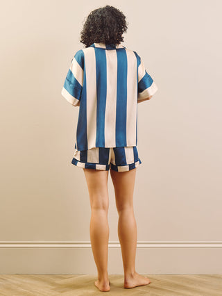 Woman wearing a blue and champagne striped short pyjamas against a beige background