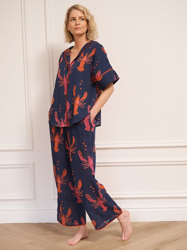 Model wearing women’s navy lobster print oversized pyjamas with short-sleeve button-up top and relaxed wide-leg trousers, photographed barefoot against a white studio wall.