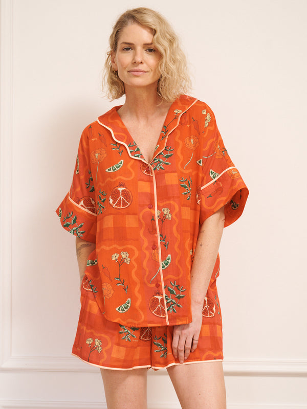 Model wearing women’s rust cotton gauze oversized shortie pyjamas with short-sleeve button-up top and matching shorts, featuring a spicy recipe print.