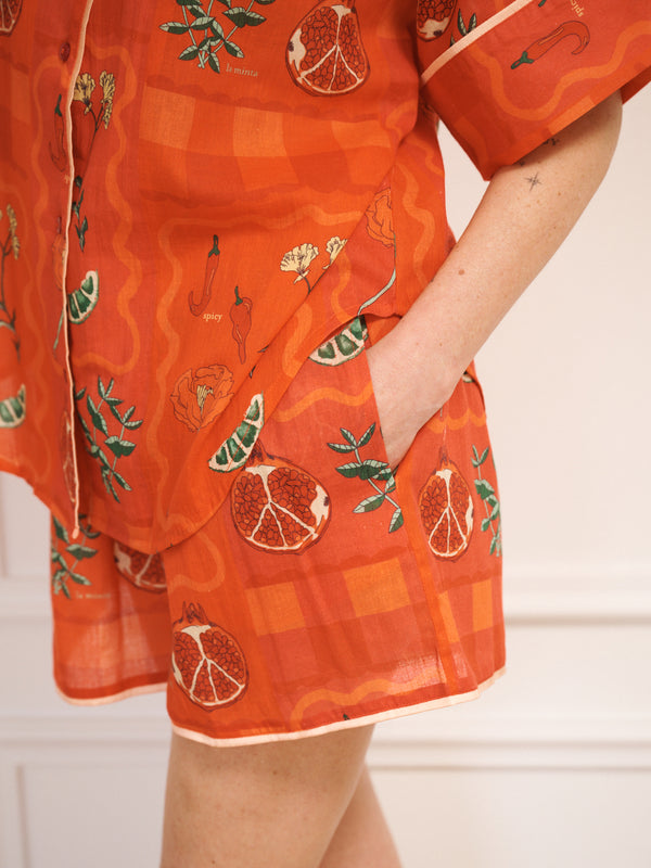 Model wearing women’s rust cotton gauze oversized shortie pyjamas with short-sleeve button-up top and matching shorts, featuring a spicy recipe print. detail shot of the pockets