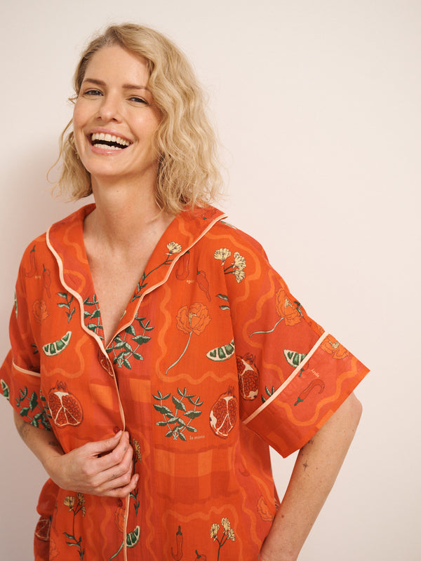 Model wearing women’s rust cotton gauze oversized shortie pyjamas with short-sleeve button-up top and matching shorts, featuring a spicy recipe print. detail shot with model laughing