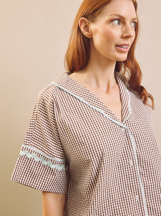 Model wears Brown Gingham check pyjama set against a beige background. Close up. 