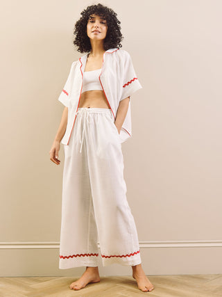 Woman wearing a white pyjama set with red accents against a plain background
