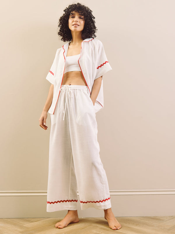Woman wearing a white pyjama set with red accents against a plain background