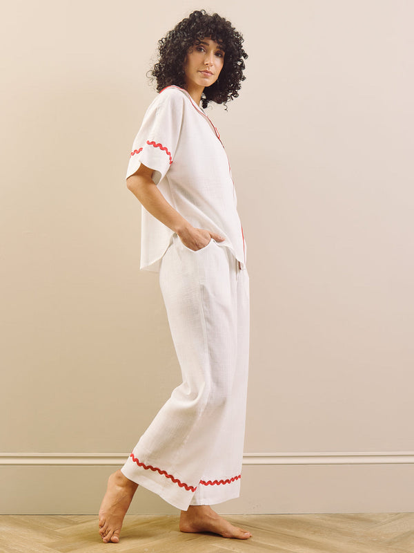 Woman wearing a white pyjama set with red accents against a plain background 