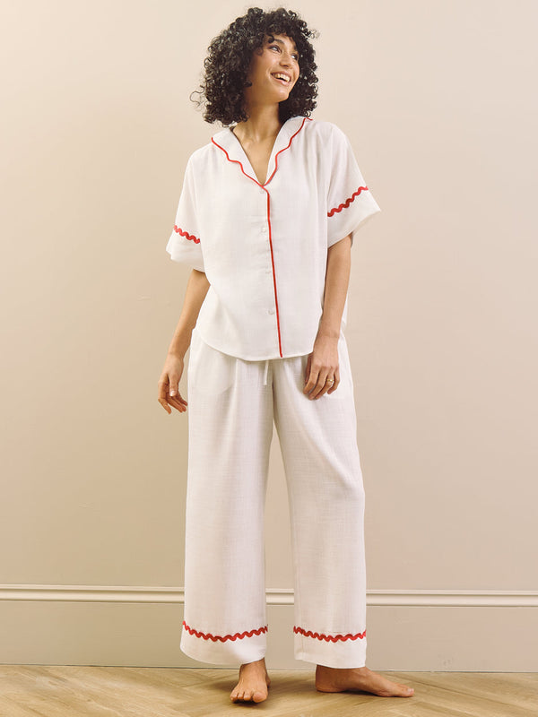 Woman wearing a white pyjama set with red accents against a plain background