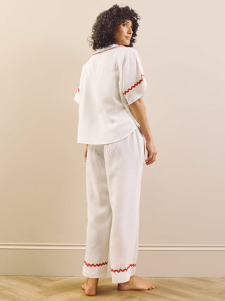 Woman wearing a white pyjama set with red accents against a plain background