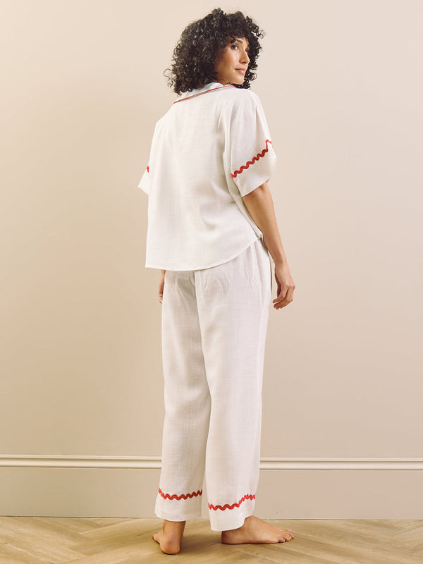 Woman wearing a white pyjama set with red accents against a plain background