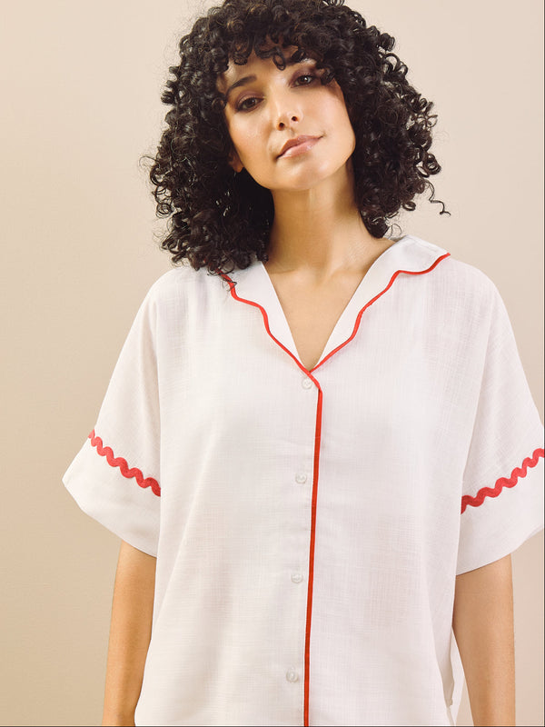 Woman wearing a white pyjama set with red accents against a plain background
