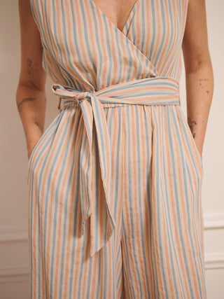 Model wearing women’s cotton gauze cross-body jumpsuit with baby pastel stripe, featuring a wrap front bodice, tie waist and wide-leg trousers. Tie belt detail