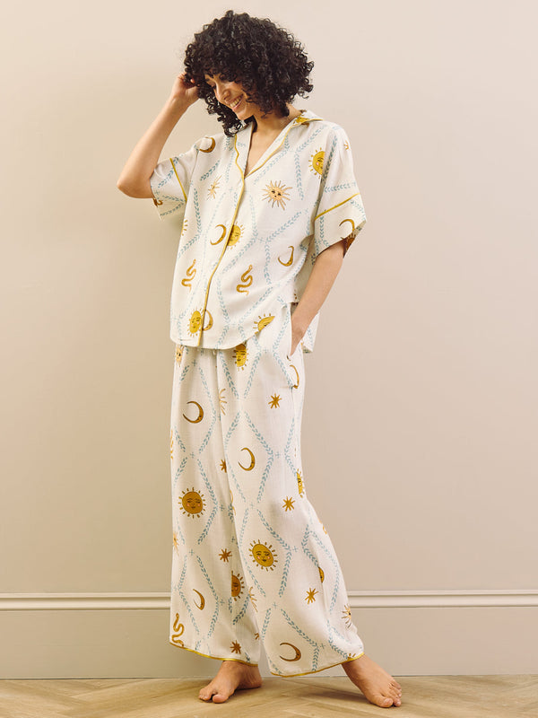Woman wearing a white pyjama set with celestial pattern against a beige wall.