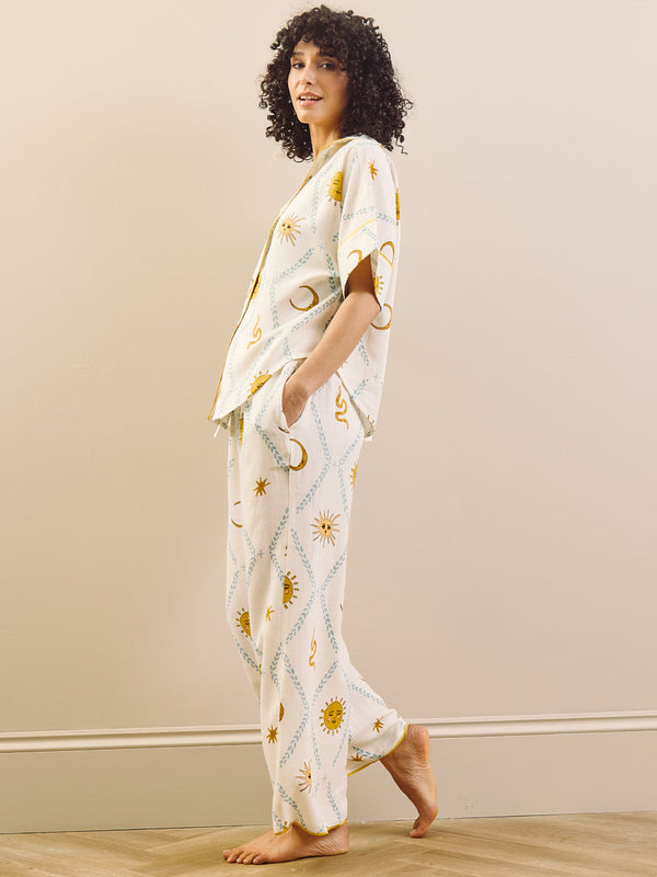Woman wearing a white pyjamas with yellow patterns standing in a room with a beige wall and wooden floor.