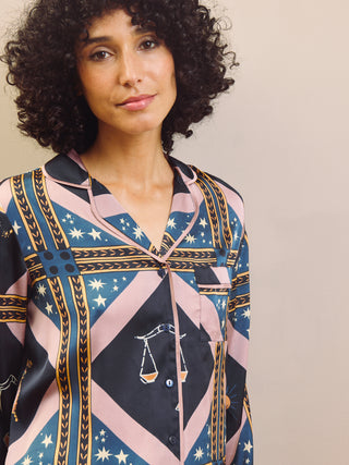 Woman wearing a celestial patterned satin pyjamas standing against a plain wall.