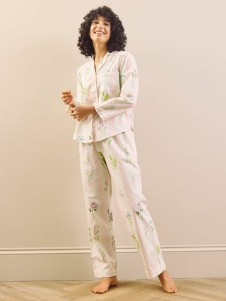 Woman wearing a long floral pyjama set standing in a room with a plain wall and wooden floor.