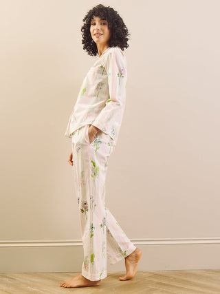 Woman wearing a white floral long pyjama set standing against a plain wall.