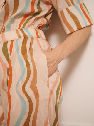 model  wearing a cotton voile smart collar jumpsuit in oatmeal Rainbow Waves print with short sleeves and wide legs. pocket detail. 