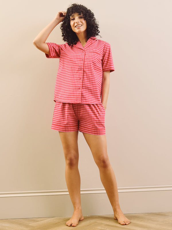 Woman wearing a red gingham short pyjama set standing against a plain wall.